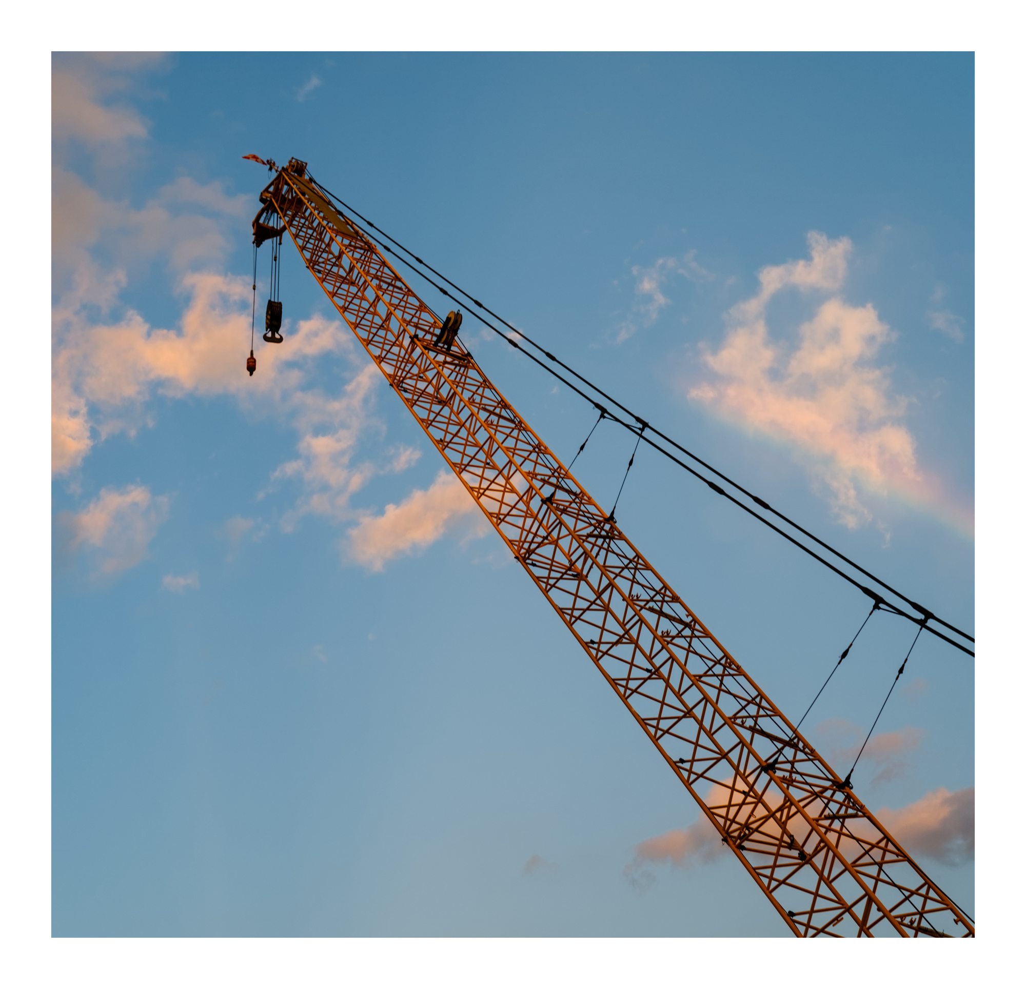A crane angled across a blue sky with warm clouds.