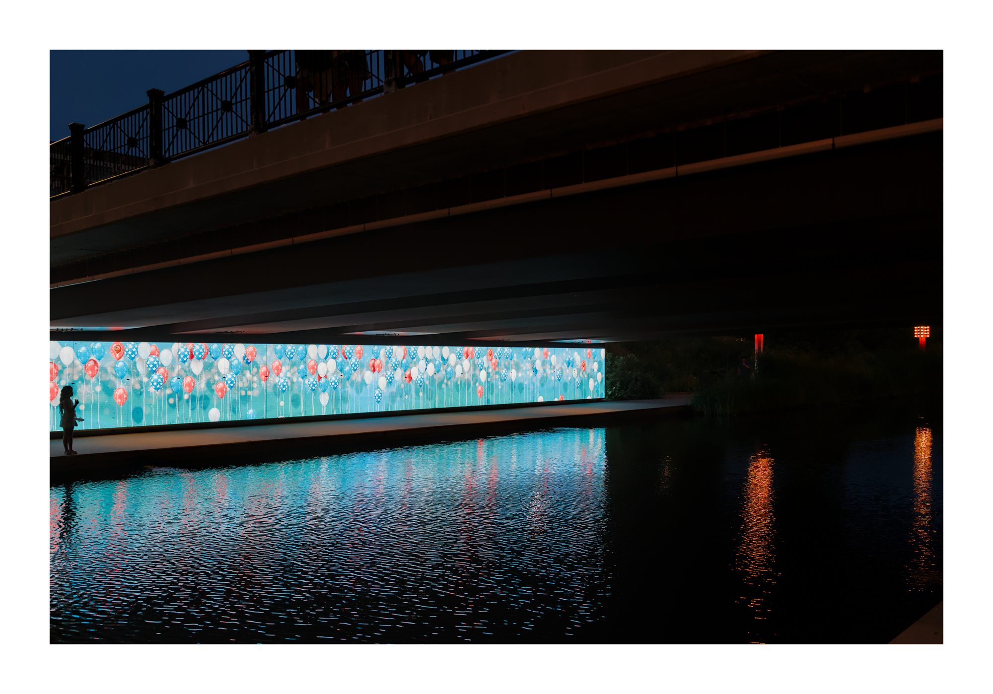 Colorful bridge lights reflected on water at night.