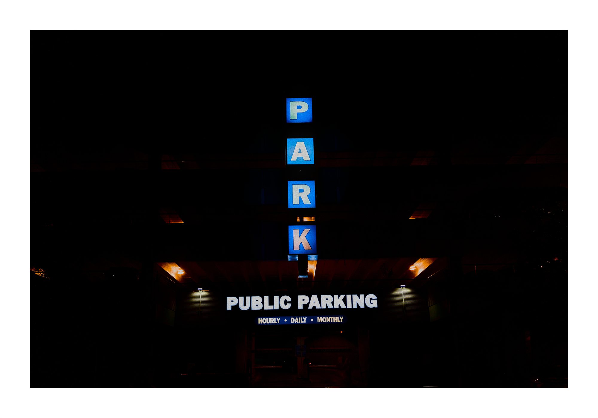 A public parking sign glowing at night.