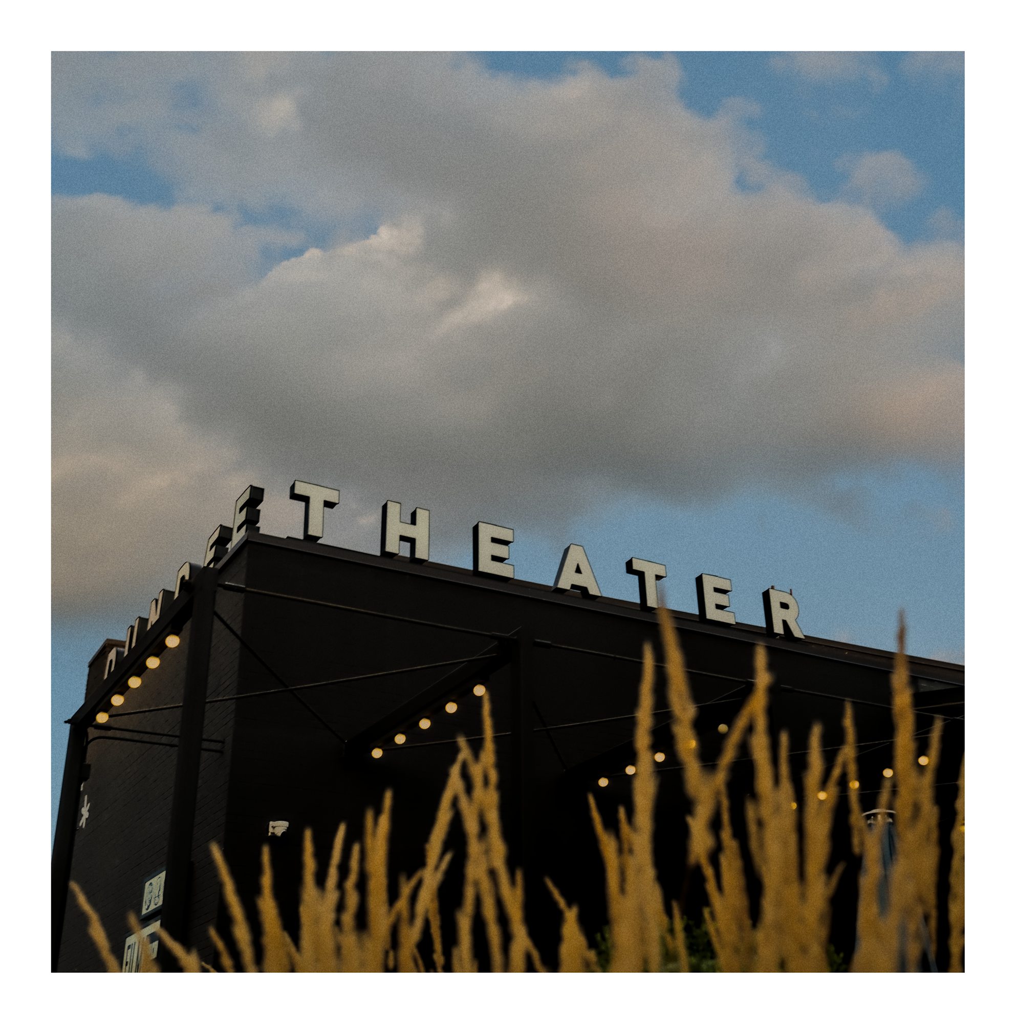 A theater sign rising above tall grass.