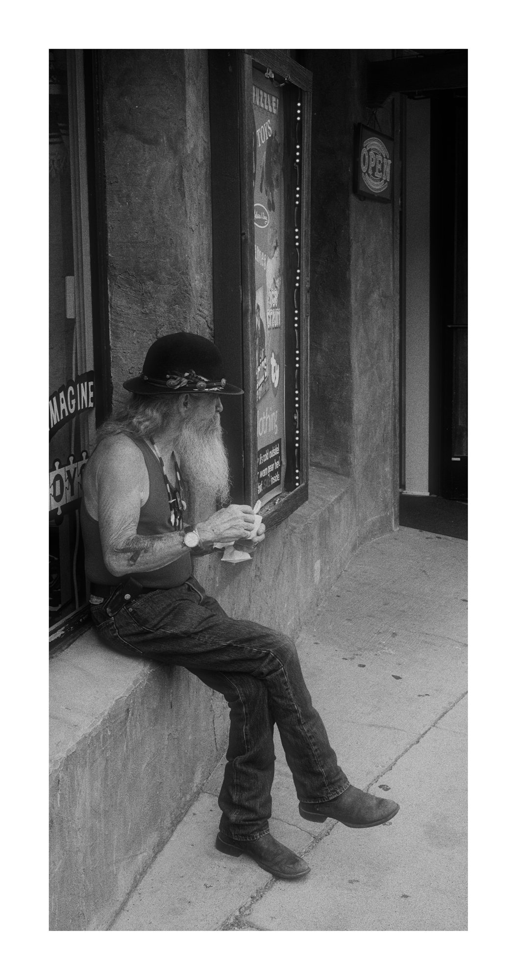 Black and white photograph of a man sitting outside a storefront.