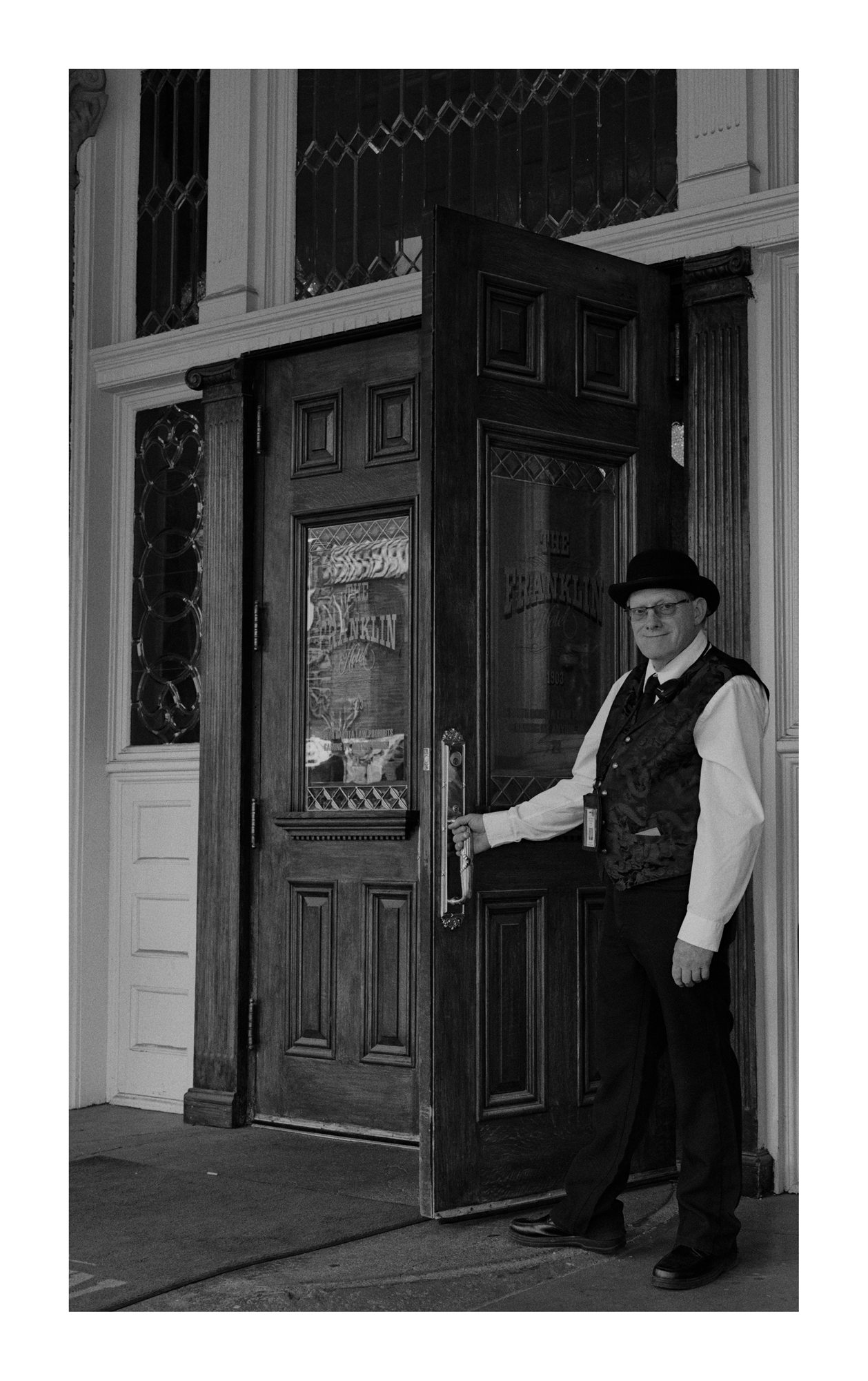 Black and white photograph of a person opening a wooden storefront door.