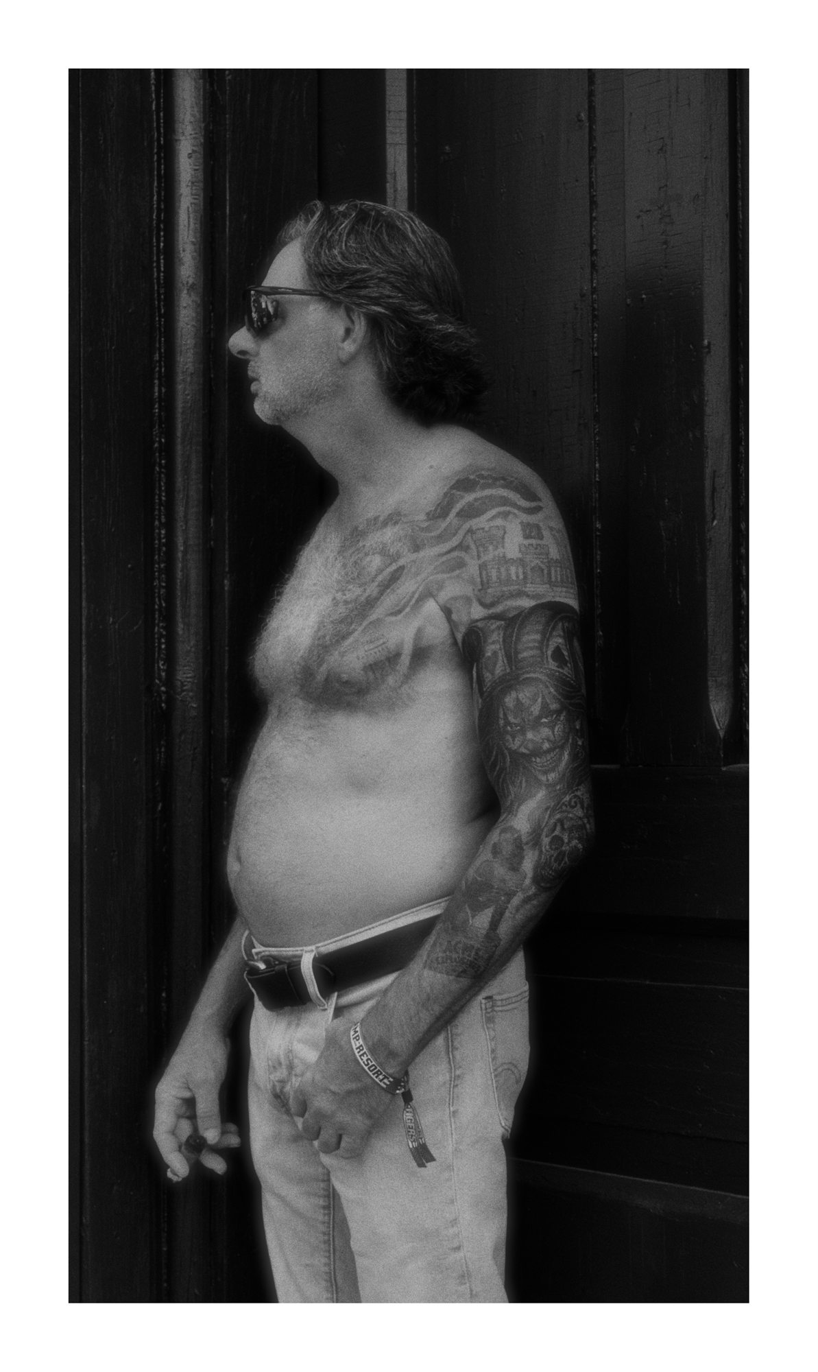 Black and white side profile of a tattooed man standing near a doorway.