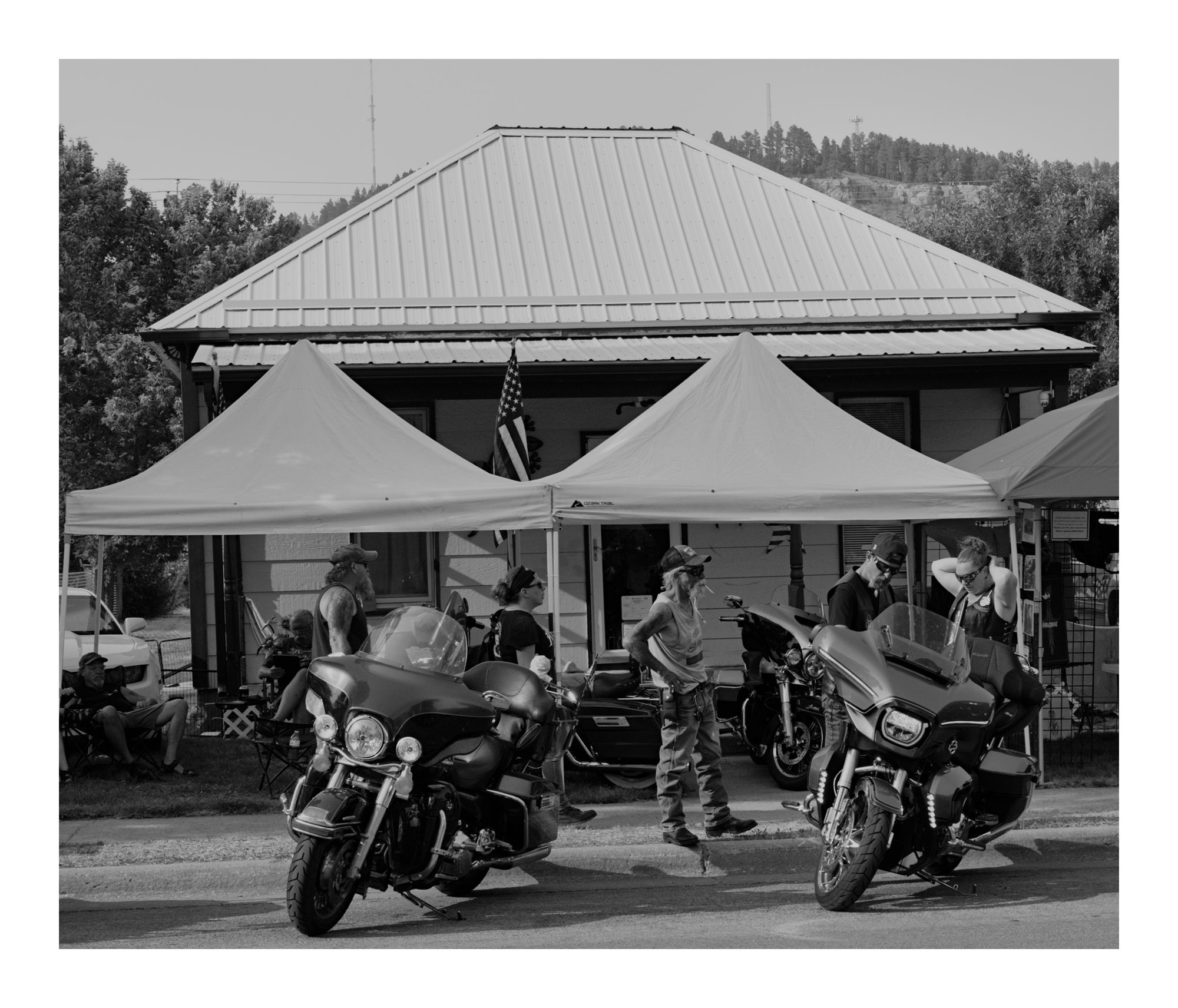 Black and white photograph of motorcycles parked beneath white tents.