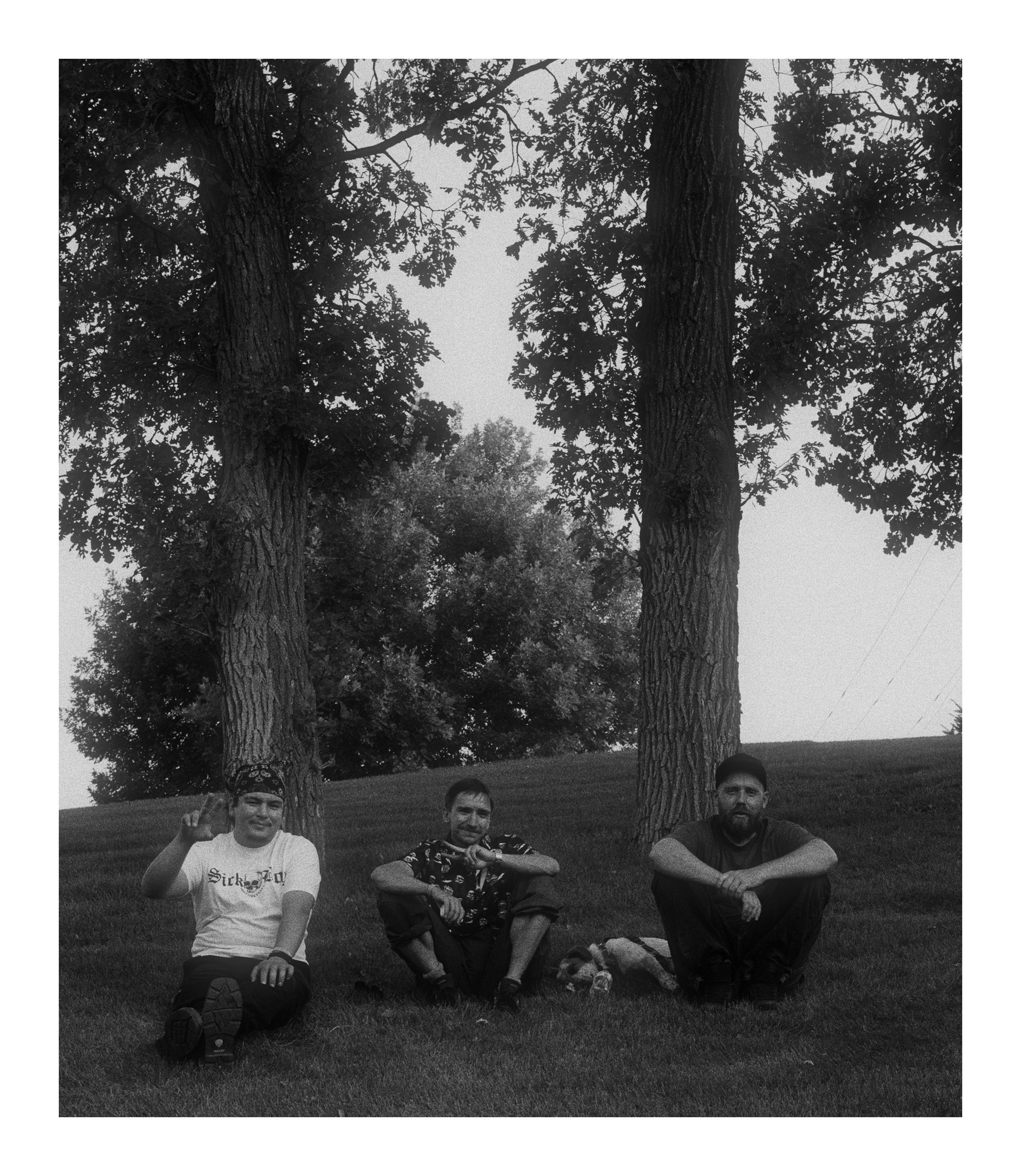 Three people sitting in hazy black and white light beneath trees.