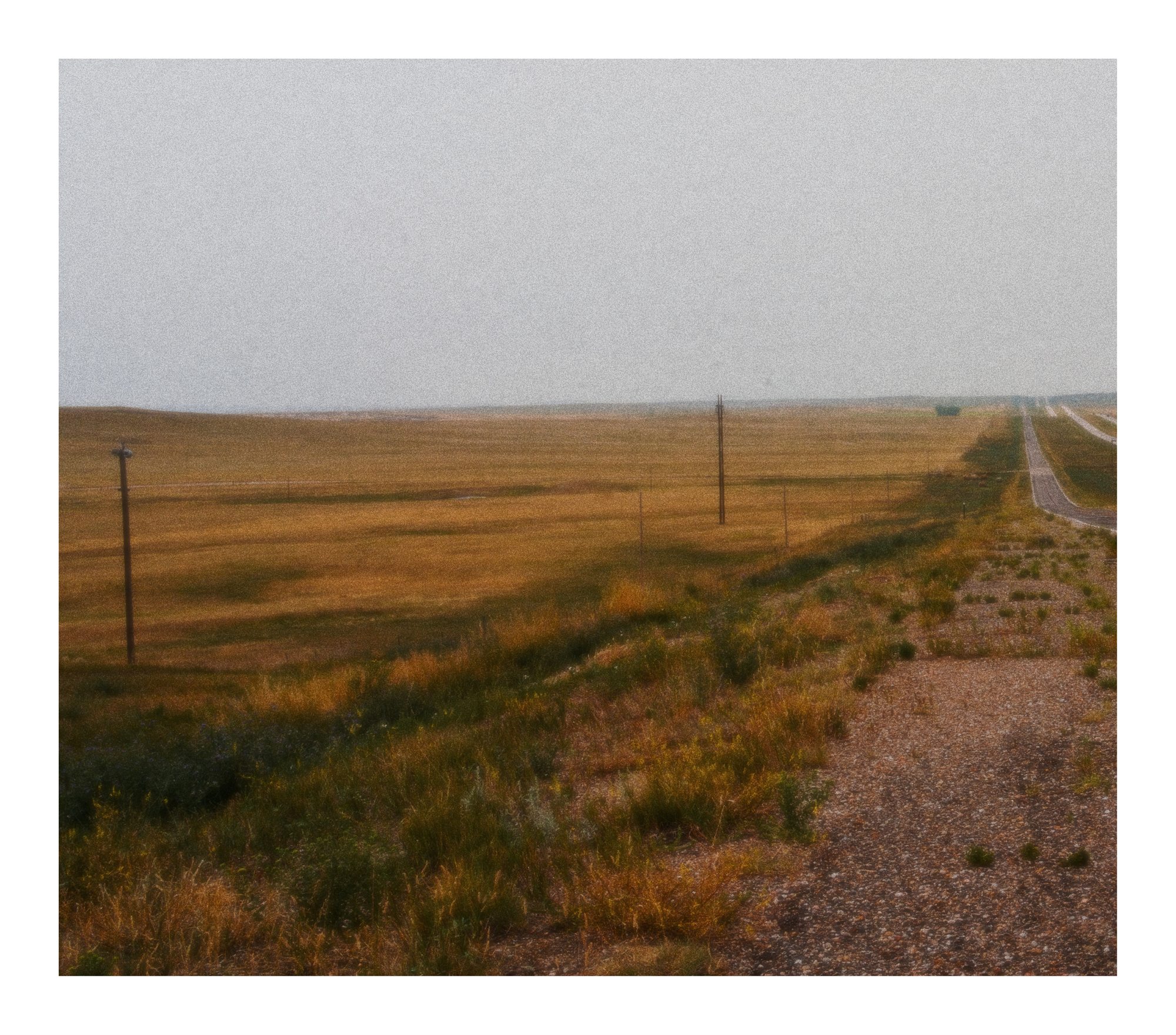 A long gravel road cutting through open prairie under a quiet sky.